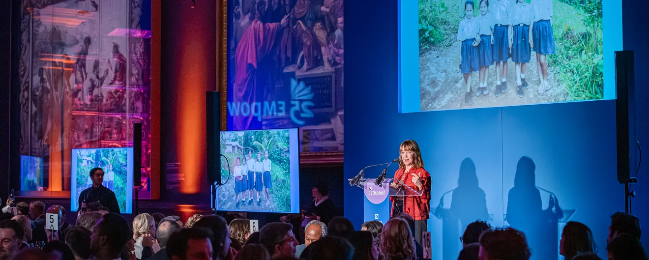 A speaker at the lectern on a blue-lit stage at the EMpower gala