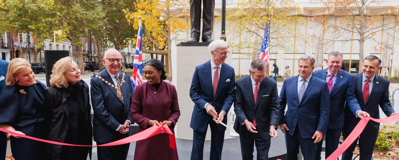 Guests and dignitaries cutting a red ribbon at a statue unveiling in a London square