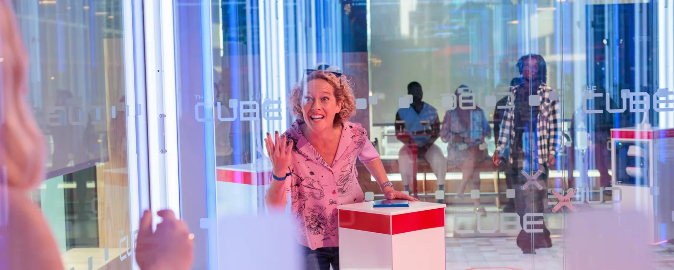 A guest laughing and waving inside the glass walls of The Cube at a VIP event