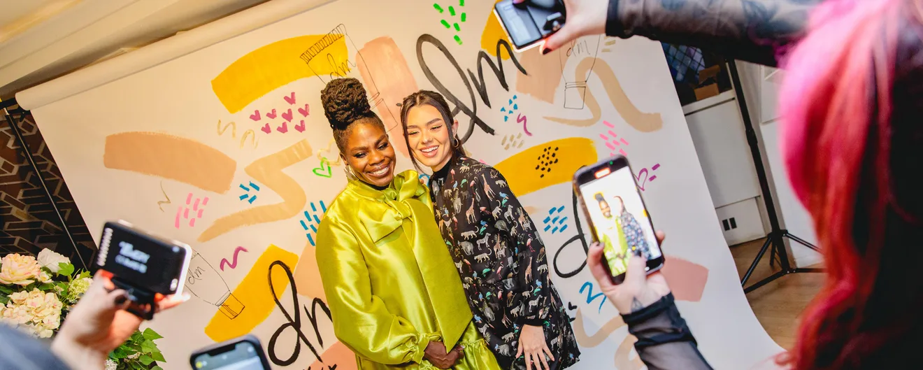 Two guests posing at a painted mural while others take phone photos