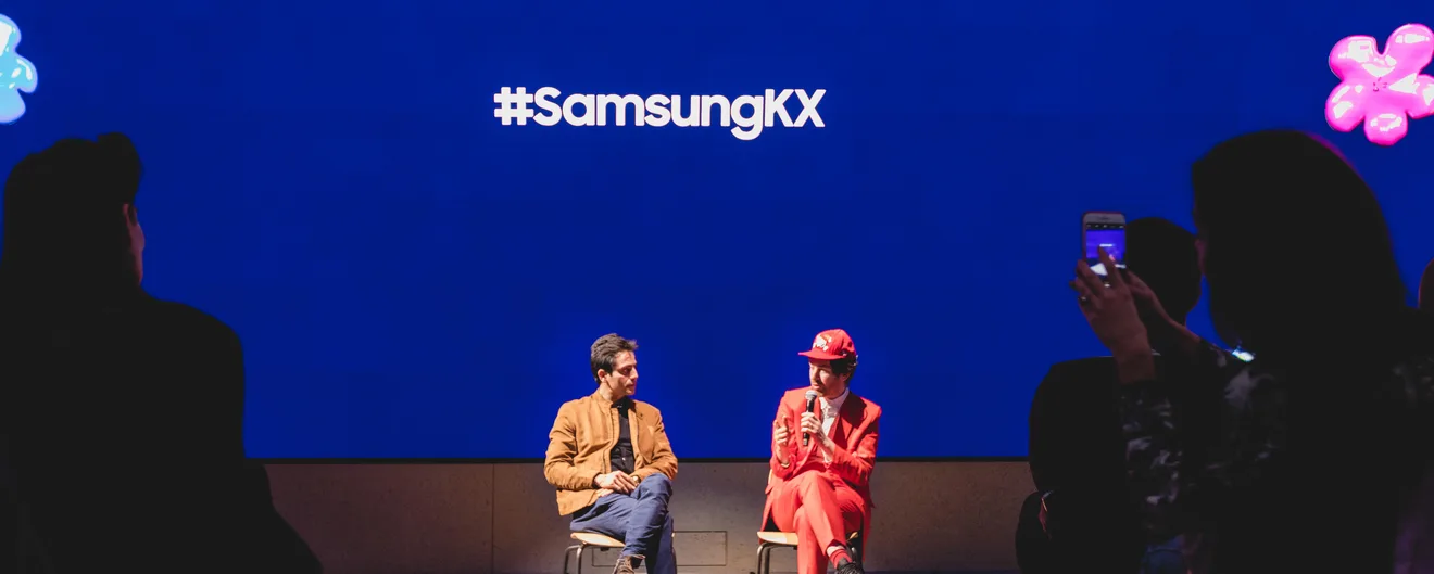 Two speakers in conversation on the Samsung KX stage, the audience in silhouette